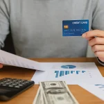 Young student sitting at a desk with a laptop and holding a card, symbolizing the use of beginner credit cards to build financial history.