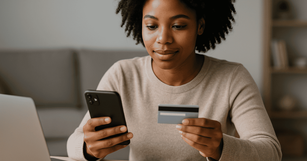 Young woman using her phone and holding a loan credit card while managing online payments at home.